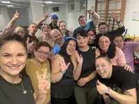 Eine große Gruppe von Teilnehmenden des Programms „Mein neues Ich #Neustart“ posiert nach einer Trainingseinheit fröhlich in einem Fitnessraum und zeigt Peace-Zeichen sowie Daumen nach oben.