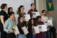 Eine Gruppe von Absolventinnen und Absolventen steht gemeinsam mit ihren Urkunden und Blumen für ein Erinnerungsfoto auf der Bühne.