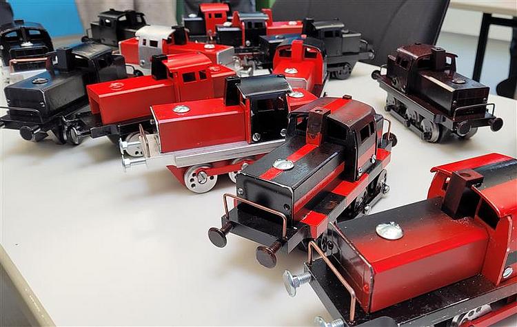 Mehrere selbstgebaute Miniaturlokomotiven aus Metall in Rot und Schwarz stehen auf einem Tisch.