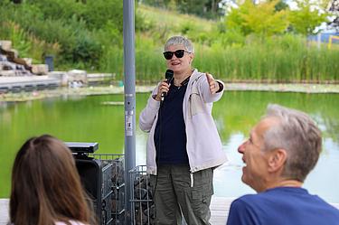 Eine Referentin begrüßt die Teilnehmenden der Nachhaltigkeitsveranstaltung am Eckert Beach vor der Kulisse des Teichs.