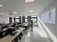 Ein Referent steht vorne in einem modernen Unterrichtsraum und hält einen Fachvortrag vor Vollzeit Studierenden der Weiterbildung zum Heizungs Sanitär und Klimatechniker. Die Teilnehmenden sitzen an Tischen und verfolgen aufmerksam die Präsentation zum Thema Sektorenkopplung und energieeffiziente Gebäudetechnik.