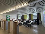 Eine Gruppe von Teilnehmenden sitzt in einem Klassenraum und folgt einer Präsentation zum Thema Nachhaltigkeit.