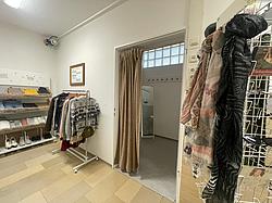 Fairschenkladen Teilansicht des Fairschenkladens. Man sieht einen Aufssteller mit Schals und CDs, eine Kleiderstange und ein Regal mit weiteren Klamotten. Auf der einen Wandseite befindet sich eine Umkleide. Der Vorhang ist halb offen und man sieht in die leere Kabine hinein.