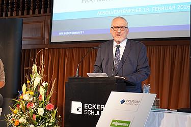 Thomas Skovronek bei seiner Rede im Rahmen der Absolventenfeier 2026 Ein Mann im dunklen Anzug hält am Rednerpult der Eckert Schulen eine Rede bei einer Absolventenfeier.
