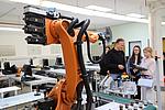 Industrieroboter in einer Werkhalle, im Hintergrund stehen Schülerinnen.