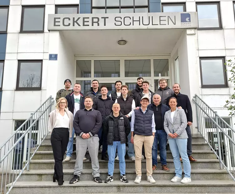 Eine Gruppe von angehenden Industriemeistern steht gemeinsam mit zwei Dozentinnen vor dem Gebäude der Eckert Schulen in Regensburg auf einer Treppe und blickt in die Kamera.