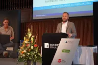 Bernhard Heinisch spricht bei der Absolventenfeier 2026 der Eckert Schulen Ein Mann im grauen Anzug steht am Rednerpult der Eckert Schulen und hält eine Ansprache bei einer Absolventenfeier.