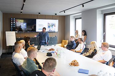 Beraten und Planen 2 Vortrag bei der beraten + planen GRUPPE mit Teilnehmer:innen an einem Konferenztisch und Präsentation im Hintergrund.