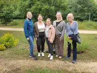 Fünf Frauen stehen lächelnd auf einem Weg im Grünen, Hintergrund mit Bäumen und Wiese