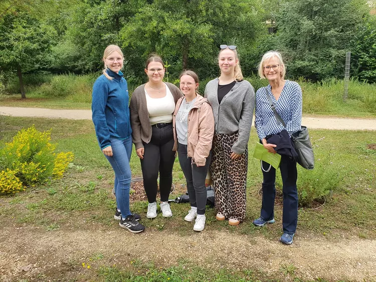 Fünf Frauen stehen lächelnd auf einem Weg im Grünen, Hintergrund mit Bäumen und Wiese