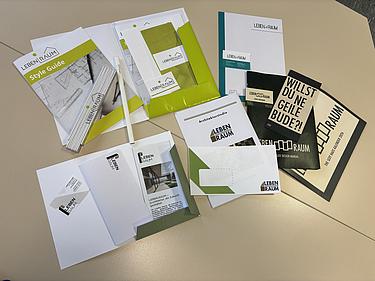 Auf einem Tisch ausgebreitete Printprodukte des Corporate-Design-Projekts „Leben.Raum“, darunter Style Guide, Briefbogen, Visitenkarten, Broschüren, Mappe und Werbematerialien.