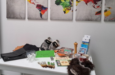 Fairschenktisch Der Fairschenktisch am Standort Kelheim der Eckert Schulen. Ein kleiner weißer Tisch bedeckt mit Büchern, Deko, CDs, Schal etc.