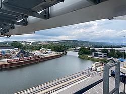 Hafenansicht mit Kränen, Eisenbahnschienen und Lagerflächen am Flussufer.