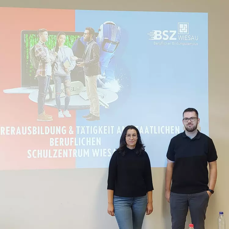 Zwei Personen stehen vor einer Präsentationsfolie des Beruflichen Schulzentrums Wiesau mit Informationen zur Zusammenarbeit in der Ausbildung.