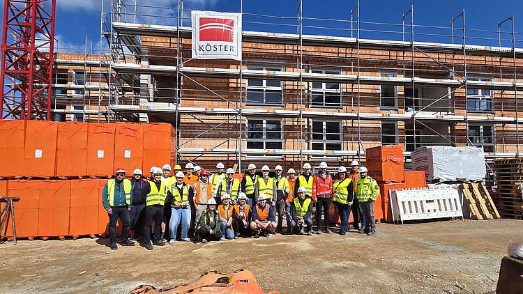 Gruppe angehender Bautechniker vor einem Wohnungsbauprojekt auf der Baustelle.