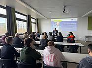 Ein Dozent steht vor einer Klasse und präsentiert Inhalte zu internationalen Bildungsangeboten auf einer Leinwand.