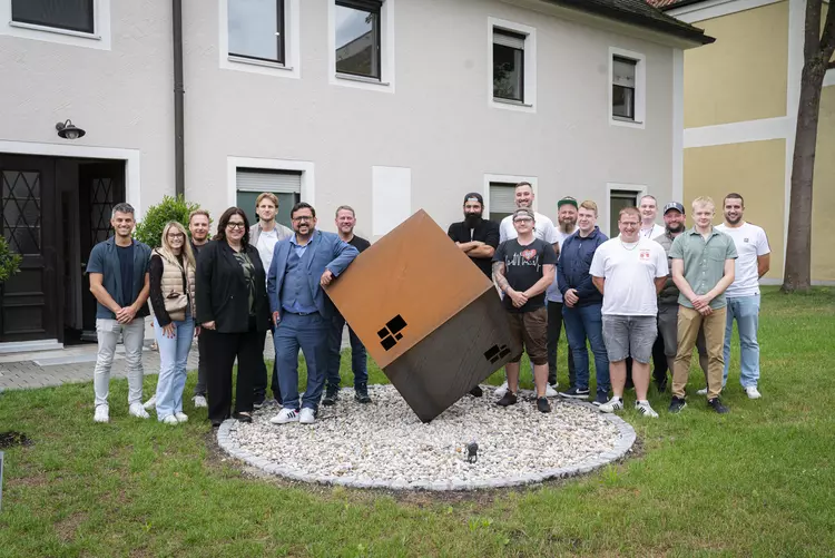 Gruppenbild vor dem Gebäude der Beraten + Planen Gruppe, im Vordergrund ein großer Hauswürfel aus Stahl als Skulptur.