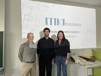 Zwei eines Ingenieurbüros und ein Mitarbeiter der Eckert Schulen stehen vor einer Präsentationsfläche mit Firmenlogo und lächeln in die Kamera.