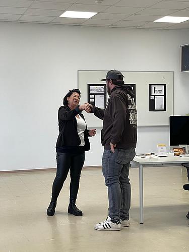 Zwei Personen stehen sich gegenüber und sprechen miteinander in einem Unterrichtsraum.