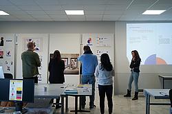 Dozentin begleitet die Abschlusspräsentation vor einer Folie mit Fazit und Projektabschluss.