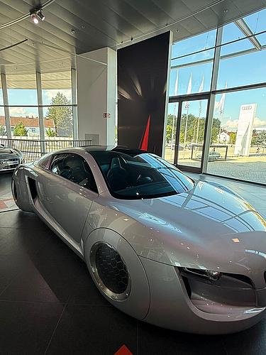 Silbernes futuristisches Audi-Konzeptfahrzeug im Audi Museum Ingolstadt, umgeben von Glasfassade und Tageslicht.