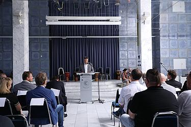 Ein Blick nach vorn: Die Rede setzt Impulse für neue Perspektiven Ein Mann im grauen Anzug spricht an einem Rednerpult mit Mikrofon im Spiegelsaal der Eckert Schulen. Im Hintergrund stehen afrikanische Trommeln auf einer Bühne. Im Vordergrund sitzen Gäste in Reihen.