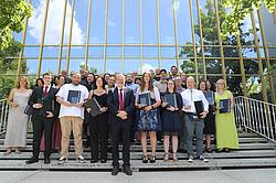Große Gruppe von Personen steht auf der Treppe vor dem verglasten Gebäude der Eckert Schulen. Viele halten Urkunden und Glastrophäen in den Händen. Die Personen lächeln in die Kamera.