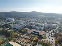 Luftaufnahme des Eckert Schulen Campus in Regenstauf mit mehreren großen Gebäuden, umgeben von Bäumen in Herbstfarben, Parkplätzen und sanften Hügeln im Hintergrund.