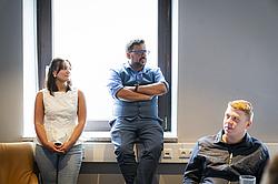 Drei Personen sitzen in einem Raum. Während ein Mann spricht hören ihm sowohl eine Frau, als auch ein Mann aufmerksam zu.