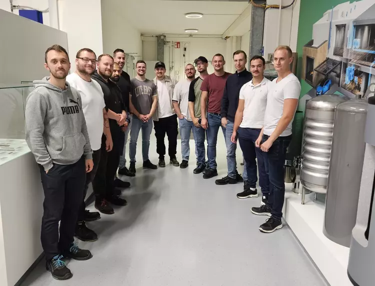 Exkursion Freiburg – Technik hautnah erleben Gruppenfoto von Exkursionsteilnehmenden in einem technischen Ausstellungsbereich mit Maschinen- und Anlagenteilen.