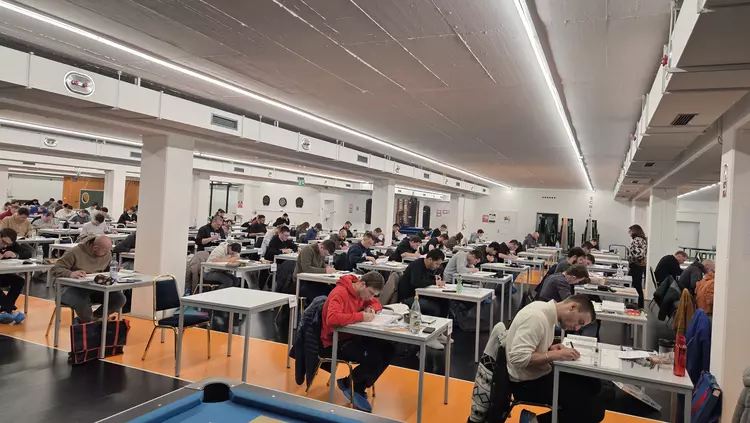 Viele Personen sitzen in einem großen Raum an Einzeltischen und schreiben konzentriert ihre Prüfung.