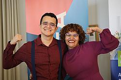 Zwei Absolventen stehen nebeneinander, zeigen ihre Urkunden und heben lachend die Arme in einer freudigen Pose.