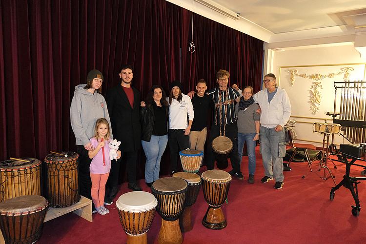 Teilnehmende der Percussion-Gruppe des BFW Eckert stehen gemeinsam mit verschiedenen Trommeln und Percussion-Instrumenten im Musikraum.