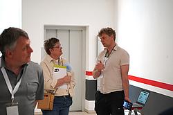 Zwei Personen im Gespräch in einem Flur, eine Person erklärt etwas mit einem Tablet.